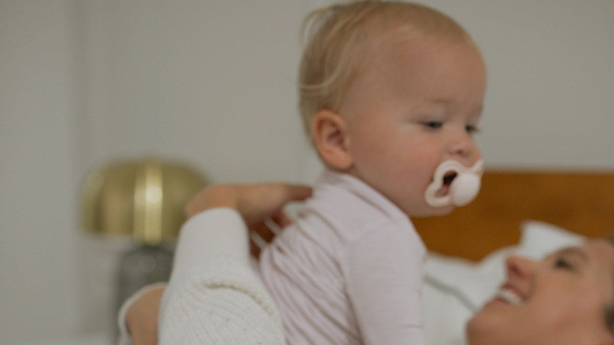 Mom laughing in bed while her baby sits up on her lap
