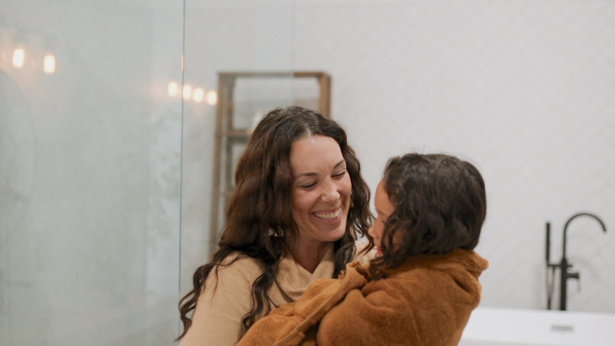 Mom smiling and hugging her little one wrapped in a towel after bath
