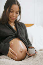 Pregnant mom smiling at her belly while holding a jar of Original Dream Cream