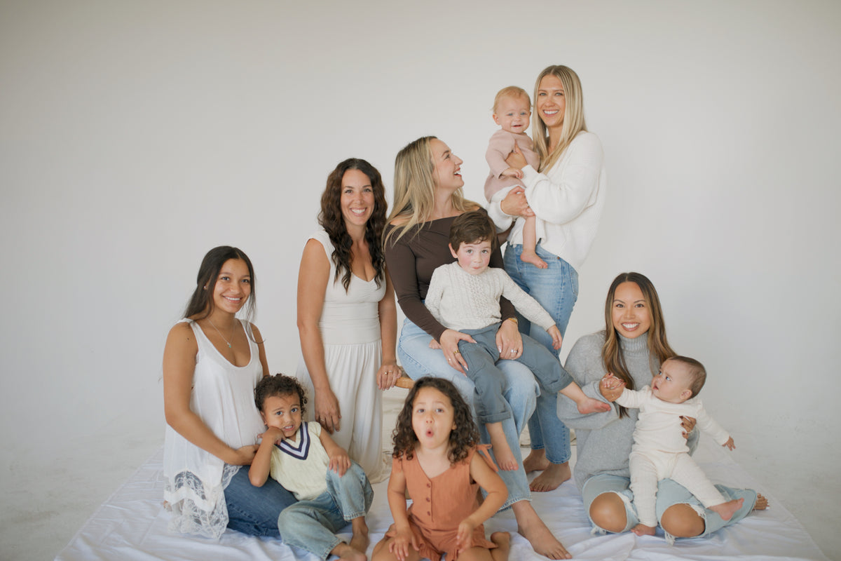 A group of moms with their babies and toddlers sitting together on a white backdrop