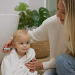 Mom applying Little Teethers roller to her baby's cheek after bath