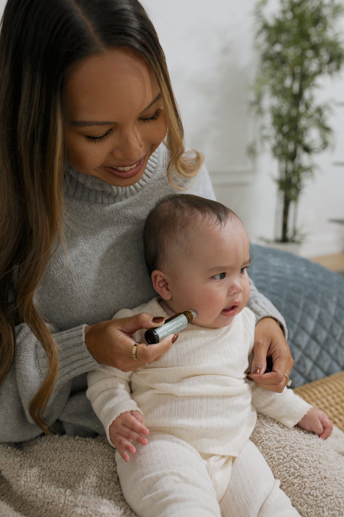 Mom rolling Little Teethers along her baby's jawline, below the ear
